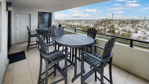 A balcony with a round table and chairs, a door, and a view of the beach.