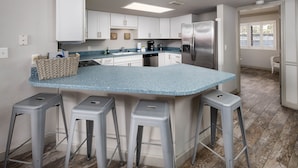 A modern kitchen with white cabinets, a stainless steel refrigerator, and a blue countertop. There are three bar stools and a basket on the counter.