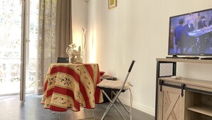A living room with a television, a table with a tablecloth, a chair, and a sliding door. - Studio Balcon, Centre Ville, Proximité Plages, Commerces, Restaurants, Musées (Antibes)