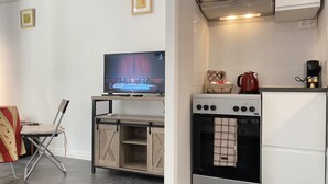A compact kitchenette with a stove, oven, and a television on a stand. - Studio Balcon, Centre Ville, Proximité Plages, Commerces, Restaurants, Musées (Antibes)