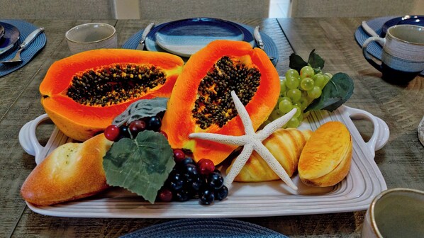 Una bandeja de frutas con papaya, uvas, bayas y carambola sobre un plato blanco.