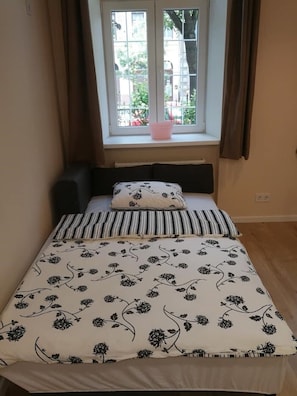 Une petite chambre avec un lit simple, une fenêtre avec des rideaux et une vue sur la verdure.