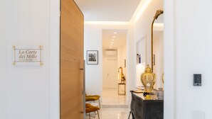 Un interior moderno con una puerta de madera, un letrero que dice "La Corte dei Mille LUXURY", una zona de comedor con una mesa negra y una lámpara dorada, y un pasillo que conduce a un baño.
