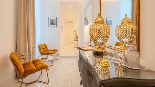 Una sala de estar moderna con una mesa de centro de vidrio, dos sillones color mostaza y un espejo grande que refleja la habitación.