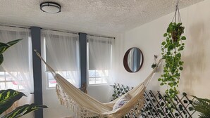 Un fauteuil suspendu dans une pièce dont le sol est recouvert d’un gazon artificiel vert, les murs sont blancs et une fenêtre est ornée de rideaux légers.