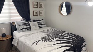 Une chambre à coucher avec un lit, un miroir rond, des tableaux encadrés accrochés au mur et un appareil de climatisation.
