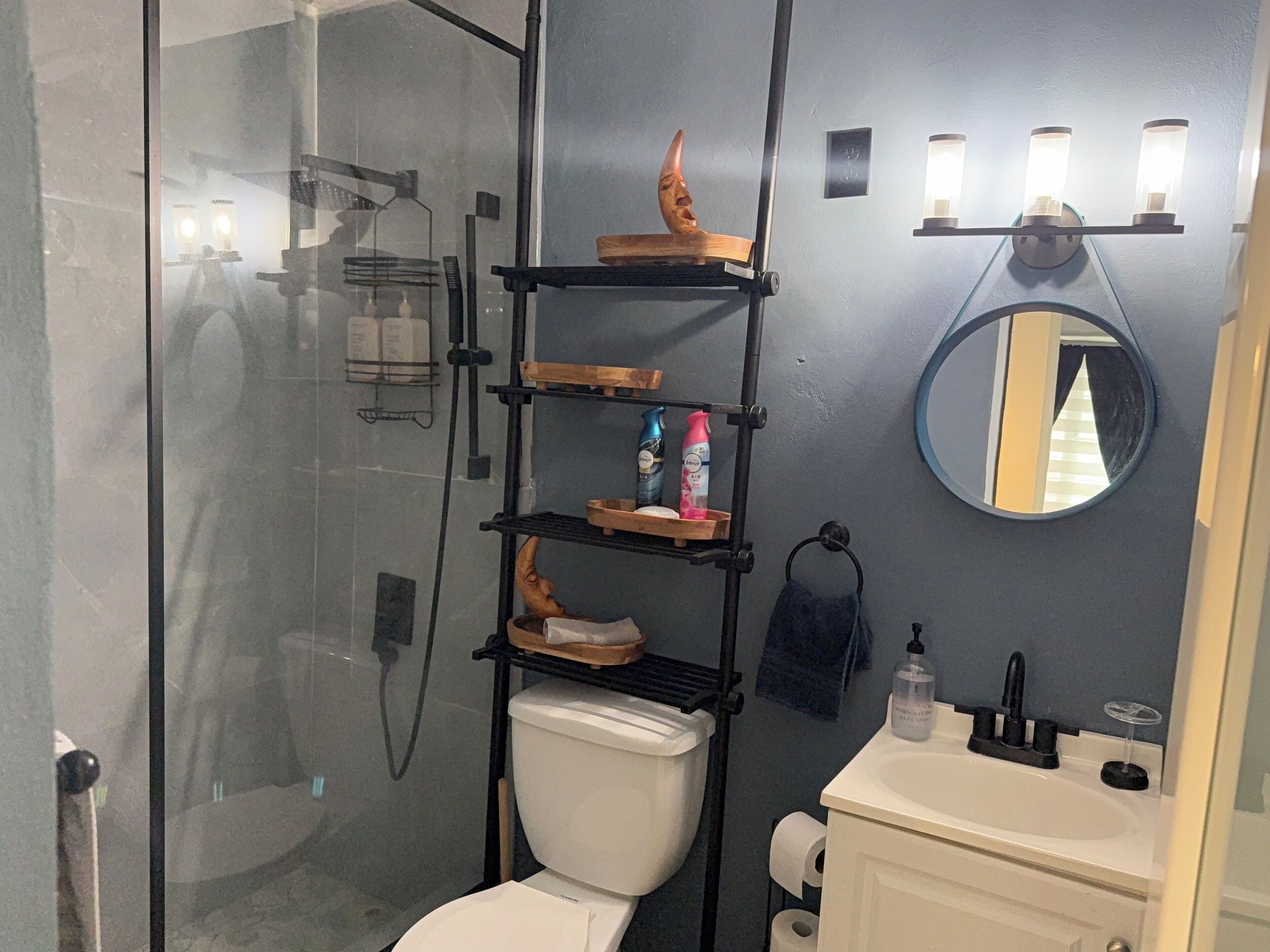 A bathroom with a glass shower enclosure, a toilet, a sink, and a vanity with shelves.