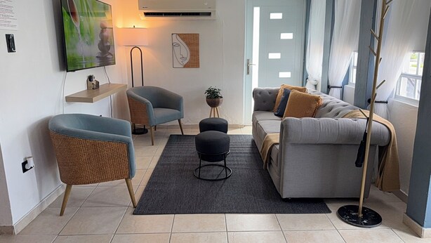 Un salon moderne avec un canapé gris, des fauteuils bleus, une table basse noire et un téléviseur fixé au mur.