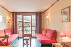 Una habitación con dos sofás rojos, una mesita de madera y vistas a un edificio y montañas a través de un ventanal.