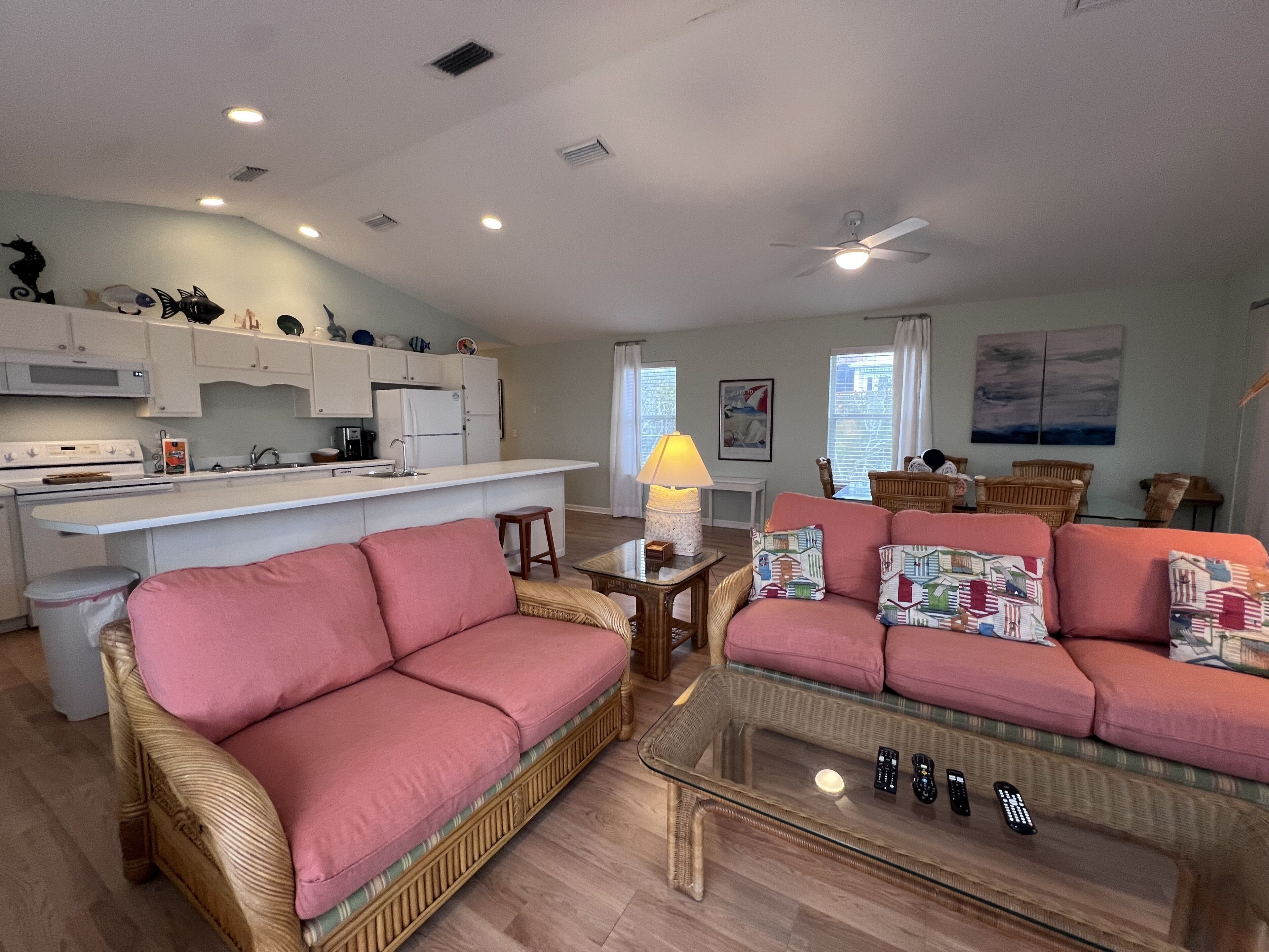 A living room with a pink sofa, a glass coffee table, and a kitchen area with white cabinets and a white stove.