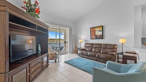 A living room with a TV, leather sofa, blue armchair, and a view of a balcony. - Lakeview Lanai in Fort Myers! Gated community with resort like amenities!!! (Fort Myers)