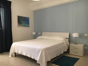 Une chambre avec un lit simple, une table de chevet, une lampe et un tableau au mur.