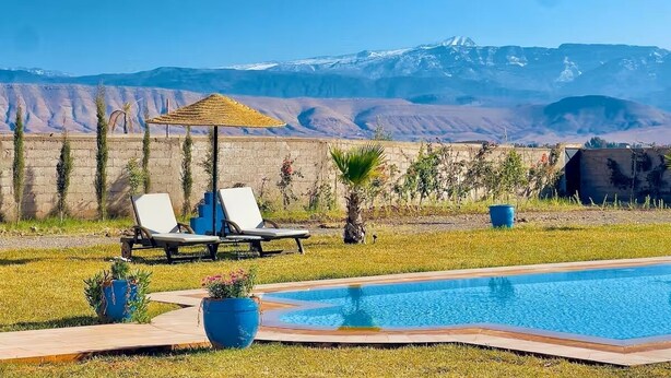 A pool area with two lounge chairs, a small umbrella, and a view of mountains in the background.