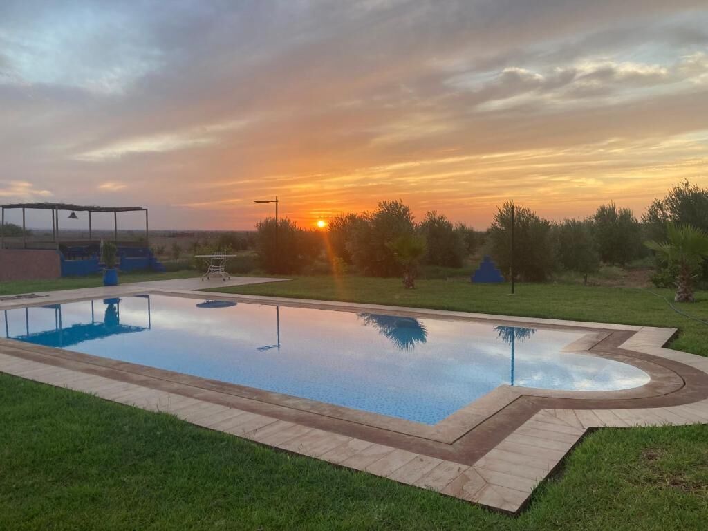 A rectangular swimming pool with a surrounding deck, set against a sunset sky.