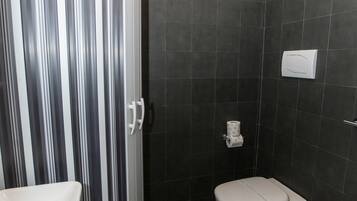 Ein Badezimmer mit Dusche, Toilette und Bidet, ausgestattet mit gestreiften Duschvorhängen und gemusterten Fliesen.