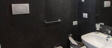A bathroom with a toilet, bidet, sink, and hairdryer mounted on the wall.