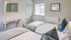 Une chambre avec deux lits, une table de chevet, un miroir, une fenêtre et un radiateur.