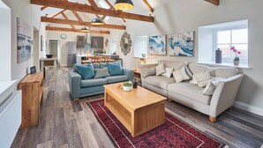 Un salon spacieux avec un plafond haut, des poutres apparentes, deux canapés, une table basse et une grande fenêtre.