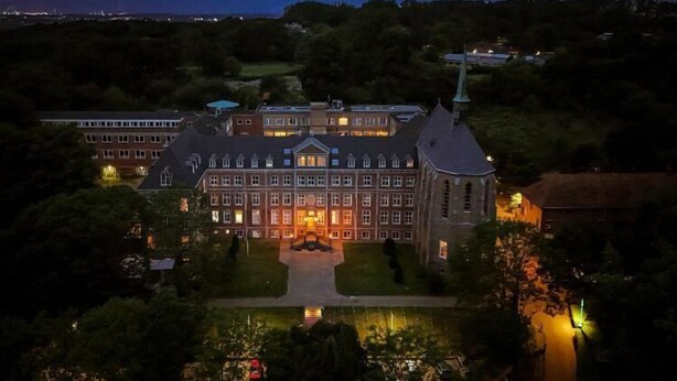 A large, historic building with multiple wings and a prominent tower, surrounded by lush greenery and a reflective water feature. - SEPHS Hotel (Sittard)