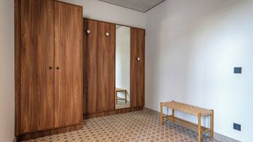 A room with a large wooden wardrobe, a small wooden bench, and patterned floor tiles.
