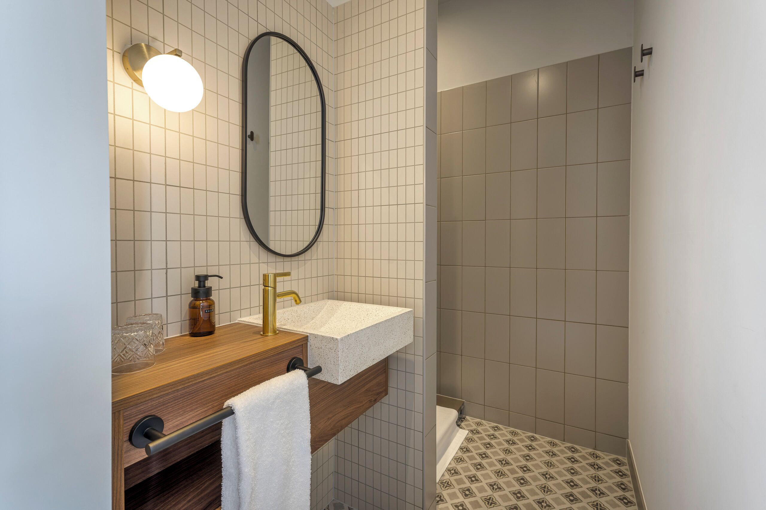 Un baño con tocador de madera, un lavabo blanco con grifo dorado, un espejo y un perchero para toallas.