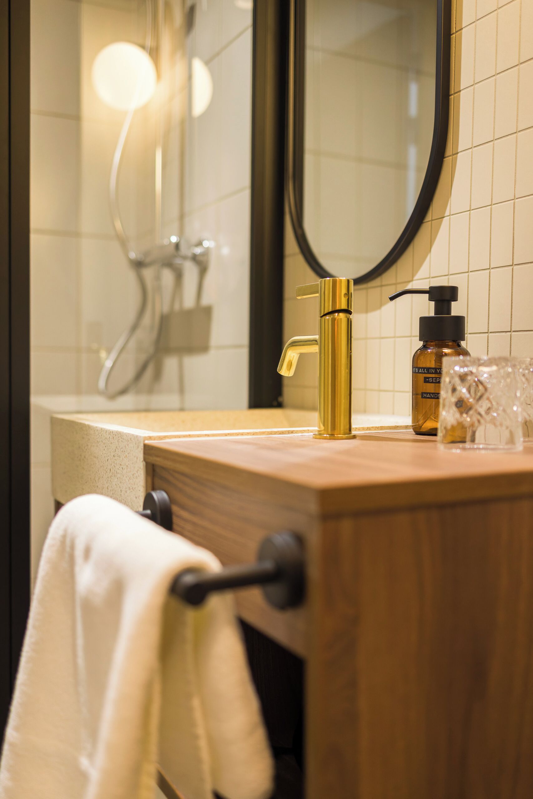 Un baño con tocador de madera, grifo dorado, espejo y ducha.