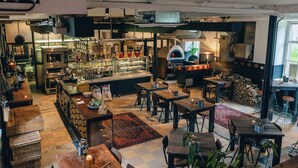 A restaurant with a kitchen area, dining tables, and a fireplace. - SEPHS Hotel (Sittard)