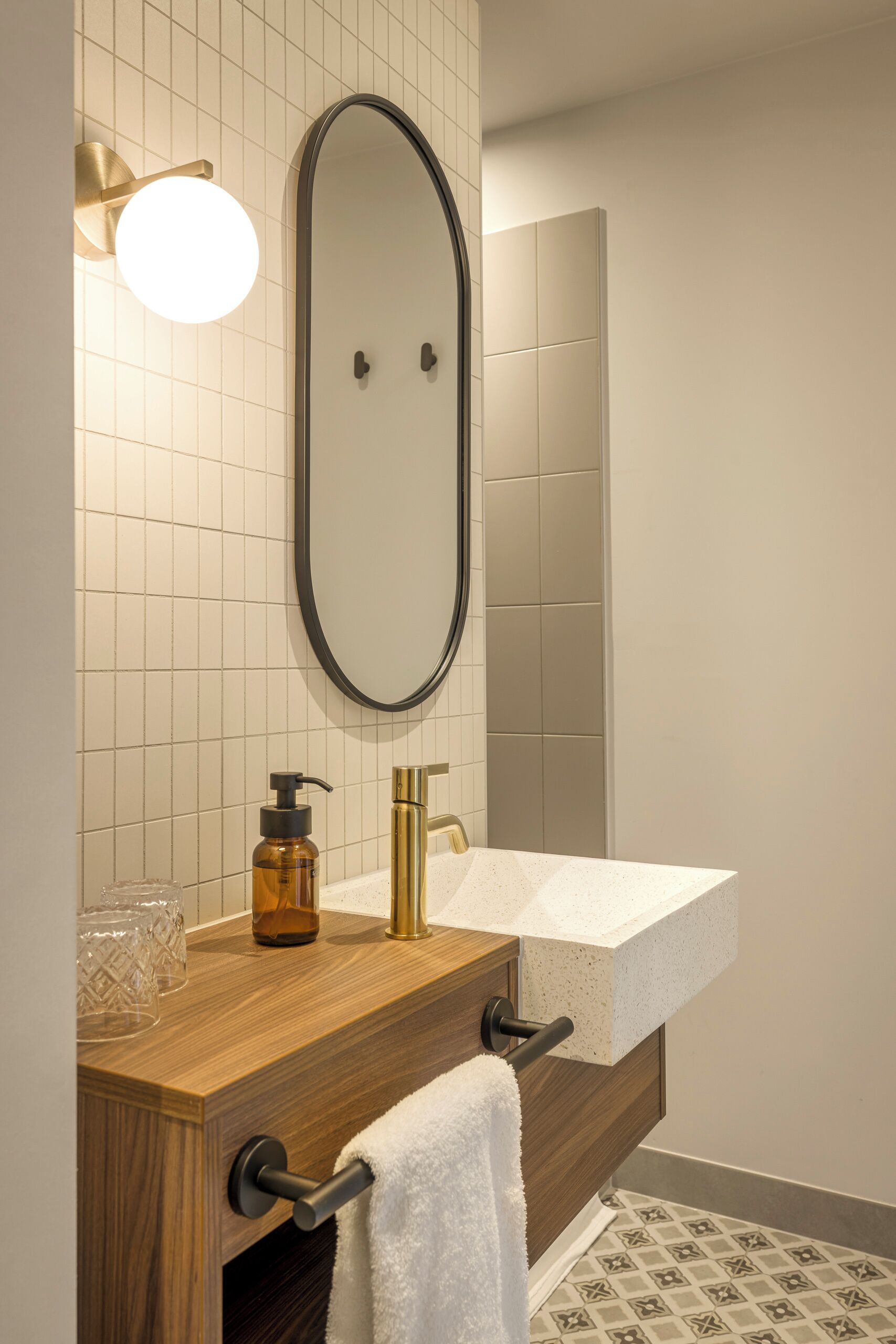 A bathroom with a wooden vanity, a white sink, a mirror, and a wall-mounted light fixture.
