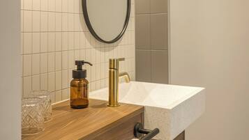 A bathroom with a wooden vanity, a white sink, a mirror, and a wall-mounted light fixture.