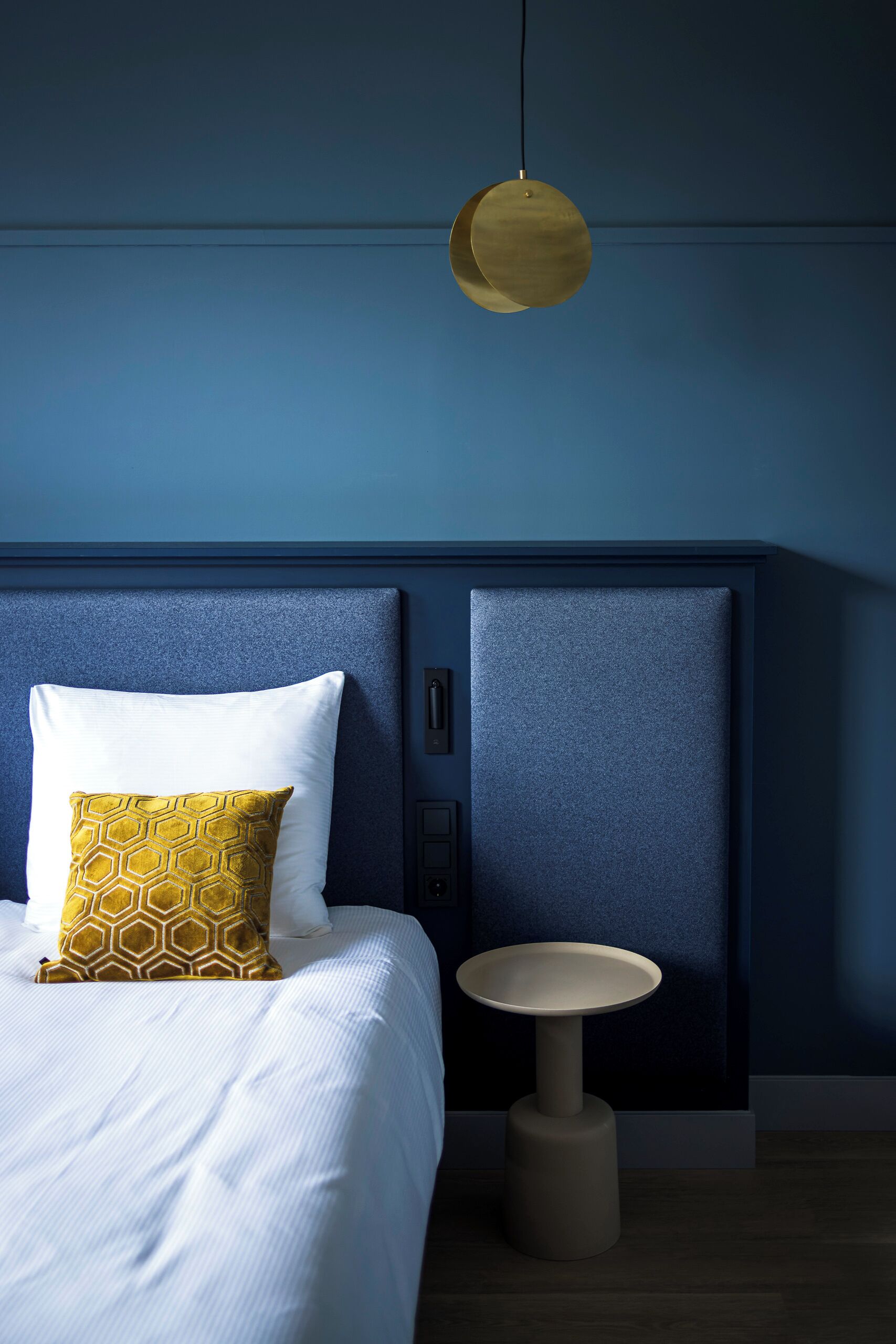 A bedroom with a bed, a bedside table, and a hanging light fixture.