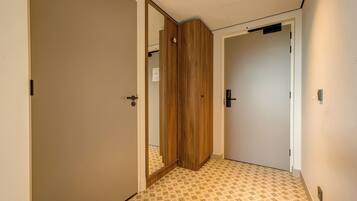 Un pasillo con piso estampado, puertas de madera y un espejo que refleja parte de la habitación.