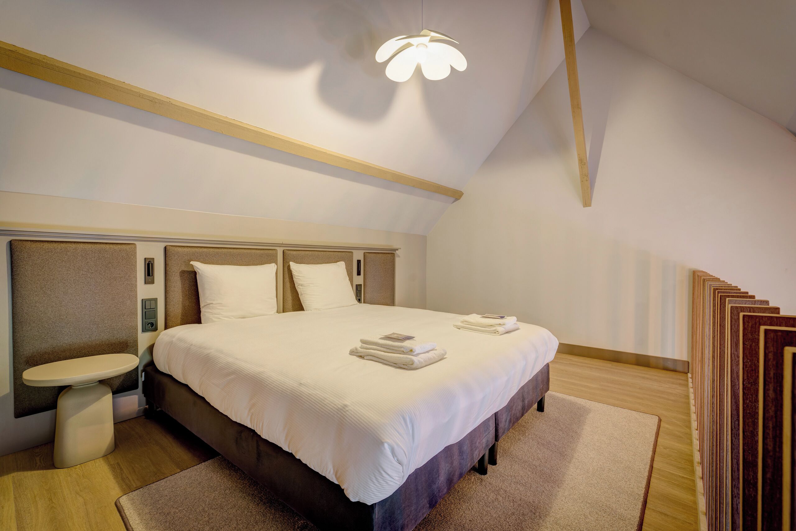 Ein modernes Hotelzimmer mit einem großen Bett, Nachttischen, einer eingebauten Sitzbank und einer einzigartigen Deckenleuchte.