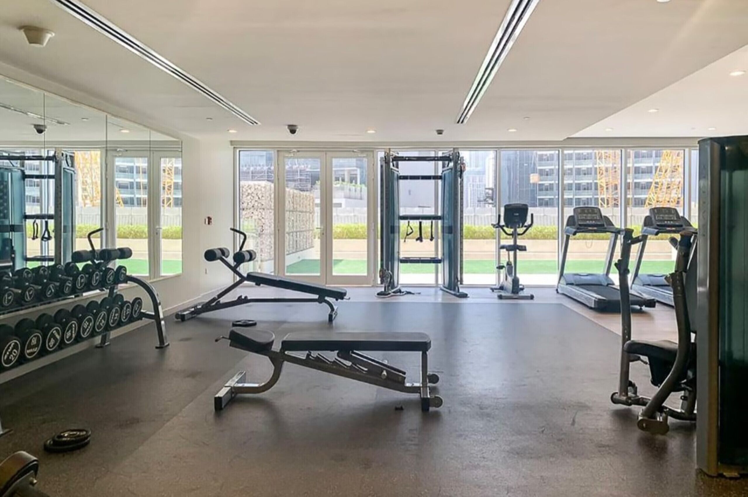 A gym with various exercise equipment, large windows, and a view of the outside.