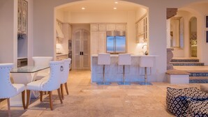 A modern kitchen with white cabinetry, a central island with bar stools, and a dining area with white chairs. - Luxurious Villas Del Mar Casita 6 with Sweeping View! (Los Cabos)