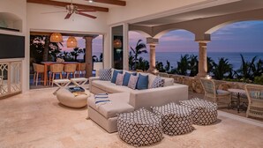 A spacious living area with a beige sofa, patterned ottomans, wicker chairs, and a view of the ocean. - Luxurious Villas Del Mar Casita 6 with Sweeping View! (Los Cabos)