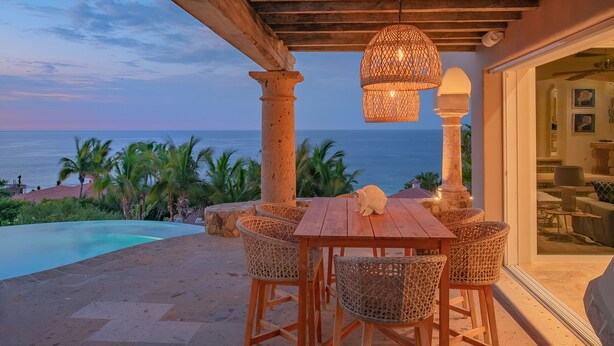 A wooden table with wicker chairs and a hanging light fixture, overlooking a swimming pool and the ocean. - Luxurious Villas Del Mar Casita 6 with Sweeping View! (Los Cabos)