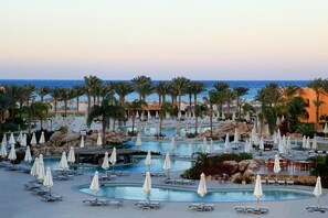 Zona de piscina en un resort con varias piscinas, sillas de descanso y sombrillas.