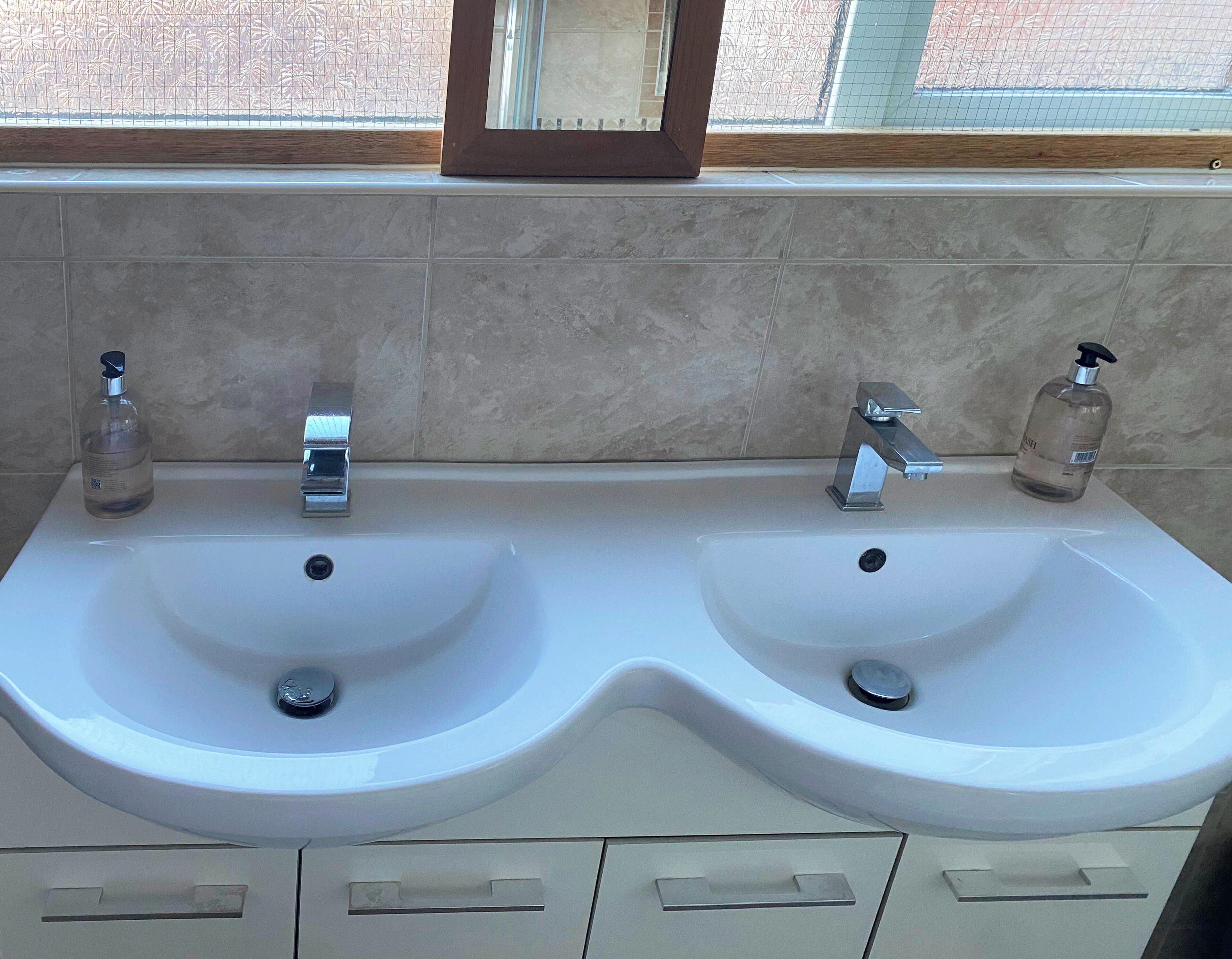 Une salle de bain avec deux lavabos, chacun équipé d’un distributeur de savon, et un miroir au-dessus.