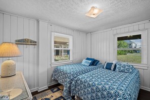 Un dormitorio con dos camas, una lámpara, una estantería con un cartel y una ventana con persianas.