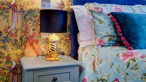 A bed with floral bedding, a blue headboard, and a nightstand with a lamp and a decorative tiger figurine. - The Peanut | East Ruston Cottages (Happisburgh)