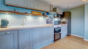 A modern kitchen with light blue cabinets, a wooden countertop, a stainless steel refrigerator, and a microwave. - The Peanut | East Ruston Cottages (Happisburgh)