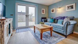A living room with a blue sofa, a wooden coffee table, and a white cabinet. - The Peanut | East Ruston Cottages (Happisburgh)