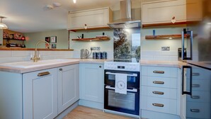 A modern kitchen with light blue cabinets, a stainless steel range hood, and a built-in oven. - Bumblebee Cottage | East Ruston Cottages (Happisburgh)