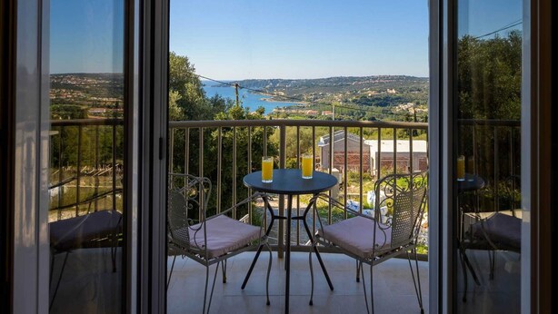 Un balcón con una mesa y dos sillas, con vistas a un paisaje pintoresco con edificios y una masa de agua.