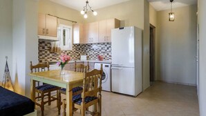 Una cocina compacta con armarios de madera, un refrigerador blanco, una mesa de comedor con sillas y una lámpara colgante.