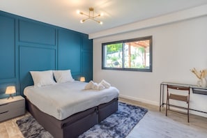 Un dormitorio moderno con una cama grande, un escritorio y un ventanal con vistas a zonas verdes.