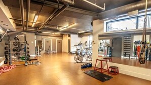 Een ruime fitnessruimte met trainingsapparatuur, een houten vloer en een groot raam.