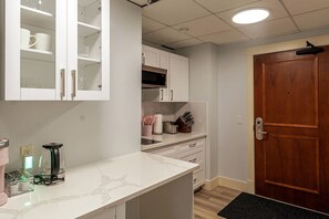 A kitchen with white cabinets, a wooden door, and a countertop with a coffee maker and utensils.