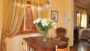 A dining area with a wooden table, chairs, a vase of white flowers, and a hanging light fixture.