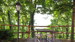 A wooden table and chairs set under a pergola in a wooded area.